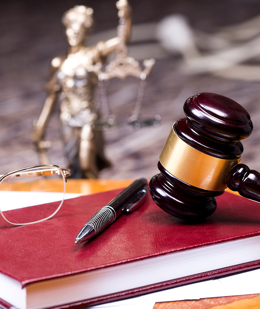 Gavel resting on top of a book with a Lady Justice statue in the background